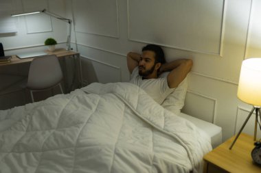 Çekici İspanyol bir adam yatağında oturuyor ve uyku sorunları yaşıyor ve gece geç saatlerde yatak odasında uykusuzluk çekiyor.