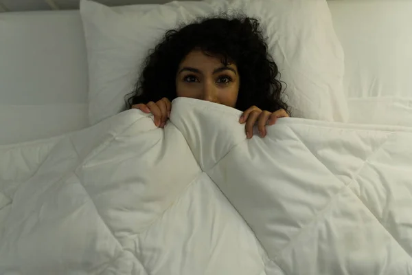 恐怖映画を見た後ベッドの中でカバーの下に隠れている怖がっている若い女性のトップビュー — ストック写真