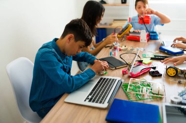 Elektronik kursu sırasında bilgisayar ve kodlama kullanan ve robot yapan genç bir çocuk.