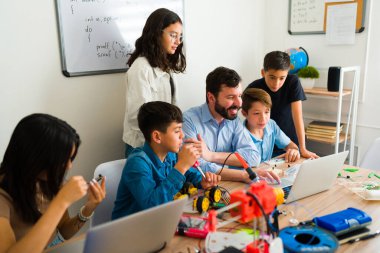 Neşeli eğitmen ve genç öğrencileri dizüstü bilgisayarda kodlama yaparken gülümsüyor ve bir robotu programlıyorlar. 