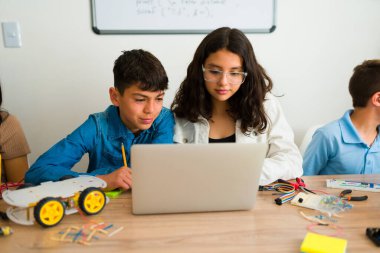 İspanyol kız ve erkek öğrenciler dizüstü bilgisayarda yazıyorlar ve kodlama dersi sırasında bir robotu programlıyorlar. 