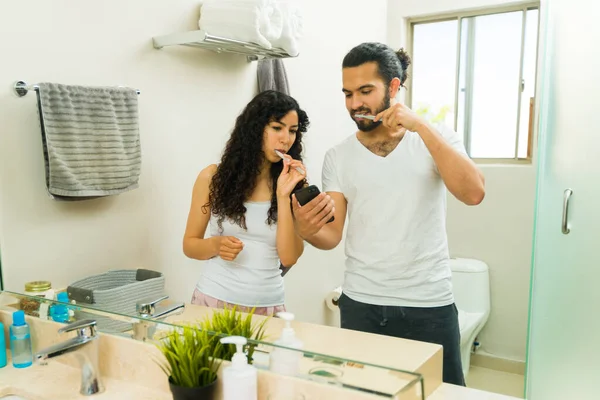 화장실에 멕시코 부부가 아침에 양치질을 하면서 스마트폰을 — 스톡 사진