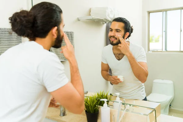 一个迷人的拉丁男人在浴室里用润肤霜做他早上的护肤例程 — 图库照片