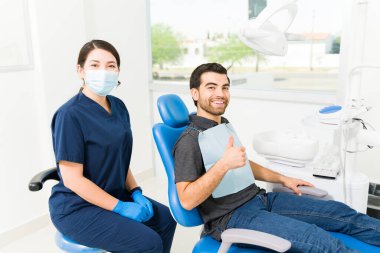 Satisfied happy male patient doing a thumbs up feeling happy with the his dental treatment after coming to the dentist clipart