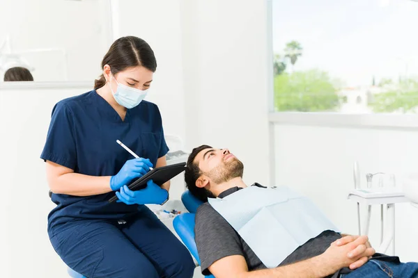 在对一名男性蛀牙患者进行检查后 带口罩的白人女牙医写下病人病史 — 图库照片