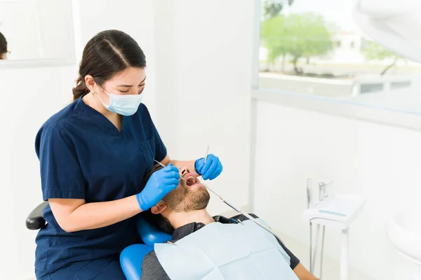 带口罩的女高加索牙医 检查男性病人的牙齿 检查蛀牙或清洁牙齿 — 图库照片