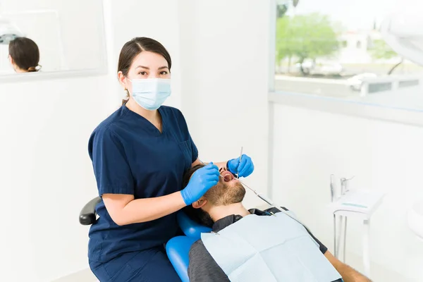 顔のマスクを持つプロの女性歯科医は 虫歯の男性患者を治療しながら目の接触を作ります — ストック写真