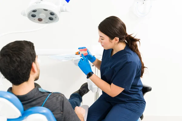 女性牙科医生在刷牙时表现出假牙 并向病人解释蛀牙的治疗方法 — 图库照片