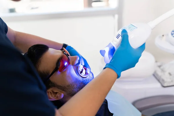 拉丁美洲的年轻人和牙医的病人正在接受美白牙齿和微笑的美白激光治疗 — 图库照片