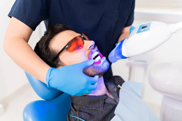 在牙医那里接受美白激光治疗的同时 还戴着安全眼镜的英俊男子 — 图库照片