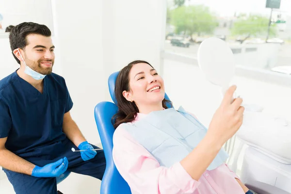 歯医者で治療や歯列矯正の後に彼女の白いまっすぐ歯を鏡で見て笑って興奮した若い女性 — ストック写真