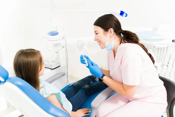 快乐的儿科牙医在做了牙齿矫正治疗后 给一位年幼的儿童病人展示了一面镜子 — 图库照片