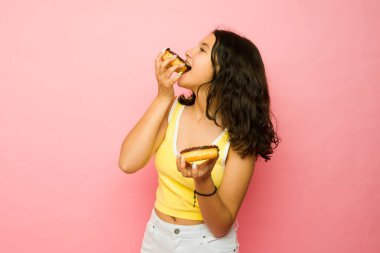 Güzel bir genç kız pembe bir stüdyo önünde lezzetli bir çikolatalı donut yemekten hoşlanıyor.