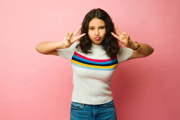 13岁的少女在粉红的背景面前做一个和平的标志 开心地打招呼 — 图库照片