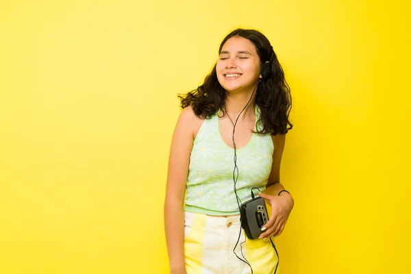 在黄色背景下听着带复古耳机的轻松自在音乐的松驰的拉丁少女 — 图库照片
