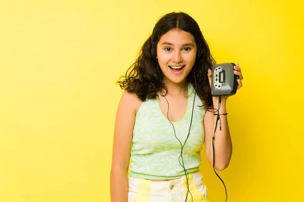 兴奋的少女展示着她的老式音乐播放器 带着耳机在黄色背景前听着一首复古歌曲 — 图库照片