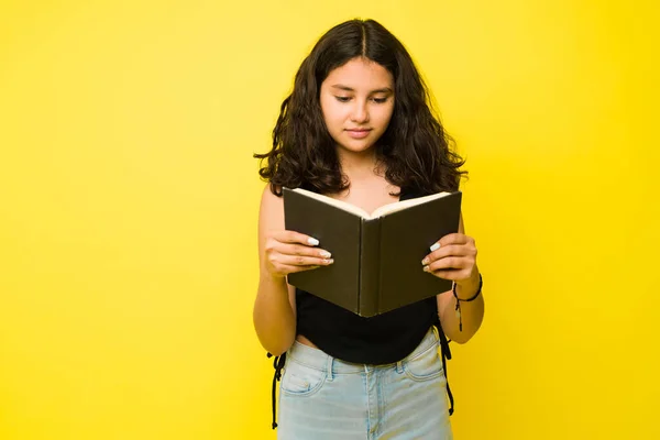 聪明的少女正在看一本有趣的书 在一个工作室里的一个黄色的广告里看起来很轻松 — 图库照片