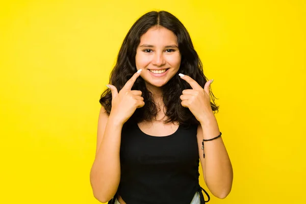 幸せな13歳ラテン語ティーンとともに大きな笑顔指す彼女の白い歯見て陽気に前に黄色の背景 — ストック写真