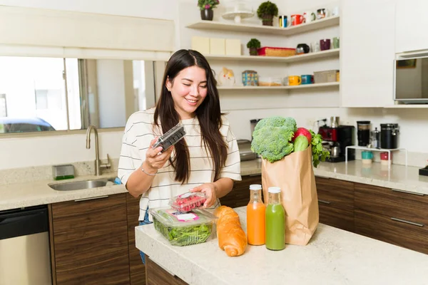 スーパーに行った後 キッチンで有機野菜や果物を取り出しながら笑顔の幸せな菜食主義者の女性 — ストック写真