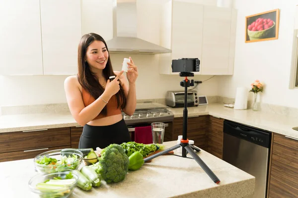 美丽健康的女人在为社交媒体拍摄Vlog视频的同时 还烹调蔬菜沙拉和服用维生素 — 图库照片