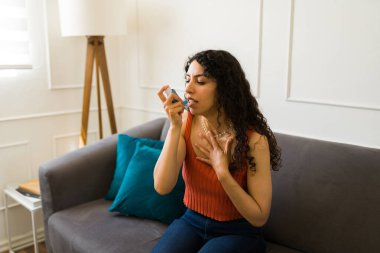 Astım krizi geçirirken astım ilacı kullanan hasta bir İspanyol genç kadın oturma odasında nefes almakta zorlanıyor.