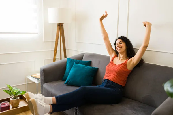 Relaxed beautiful latin woman raising her arms and relaxing while resting in the couch on her new living room home