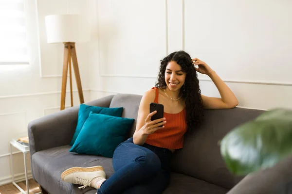 在智能手机上发短信或使用社交媒体以及在沙发上放松时 快乐的年轻女性看上去很开心 — 图库照片