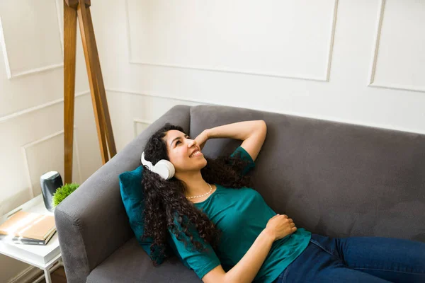 美しい女性がソファの上でリラックスし ヘッドフォンで音楽を聴きながら幸せそうな笑顔 — ストック写真