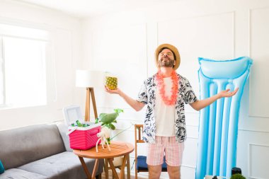 Çekici bir orta yaşlı adam ananas içeceğiyle rahatlıyor ve evinde rahat bir yaz tatili boyunca içkiyle birlikte şişirilebilir ve soğutucu kullanıyor.