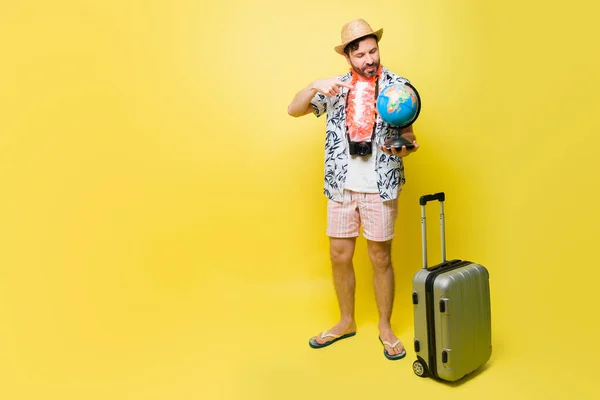휴가를 보내는 반바지를 모자를 지구를 가리키는 중반의 남자가 해변을 여행하고 — 스톡 사진