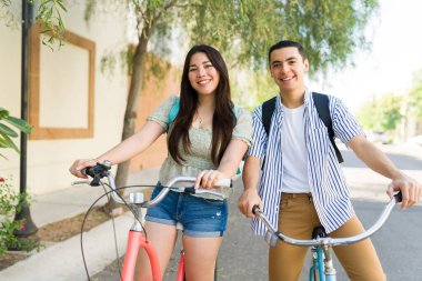 Neşeli genç çift gülerek dışarıda bisiklet sürerken ve yazın tadını çıkarırken mutlu görünüyorlar. 
