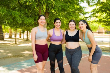 Etkinlik giysileri içinde gülümseyen çekici kadınlar parkta egzersiz yapmadan önce göz teması kuruyor ve vücut kabulünü destekliyor.