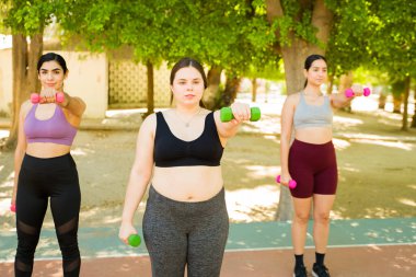 Kafkasyalı şişman kadın ve bir grup kadın arkadaş halter kaldırarak vücut kabulünü ve çeşitli vücutları teşvik ediyorlar.