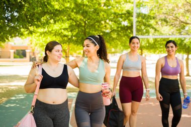 Farklı vücutlara sahip, kucaklaşan ve gülen, vücut kabulünü arttırmak için dışarıda spor yapan kadın arkadaşlar. 