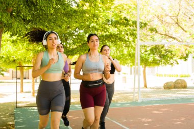 Kulaklıkla koşan Latin kökenli aktif bir grup kadın açık havada çalışırken müzik dinliyor.