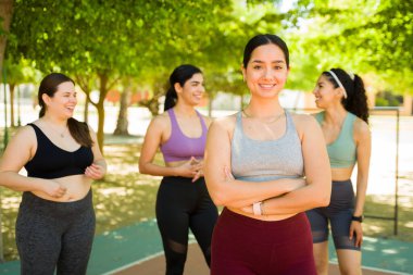 Güzel, neşeli, gülümseyen bir kadın. Farklı arkadaş grubuyla dışarıda egzersiz yaparken göz teması kuruyor.