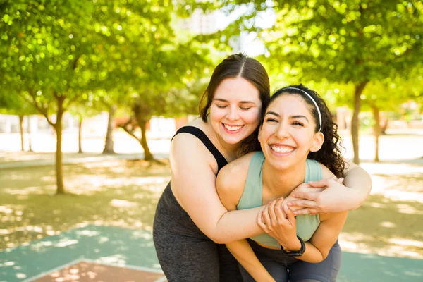 公園で一緒に運動した後の楽しさと体のポジティビティに満足しながら抱き合って笑っている興奮した女性の親友 — ストック写真