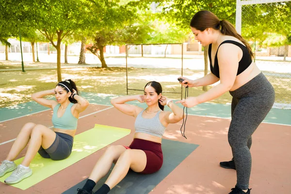 Plus size young woman training with a group of diverse women doing sit ups exercises in the park and working out promoting body positivity