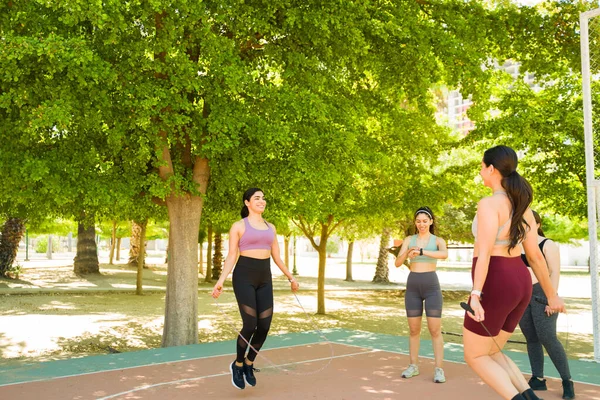 Happy group of diverse women smiling jumping rope and exercising during a cardio workout outdoors