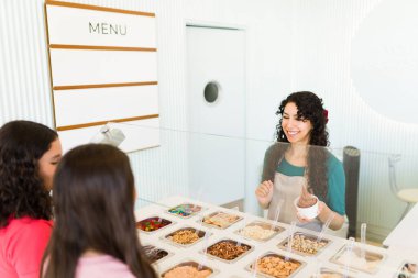 Neşeli kadın dondurulmuş yoğurt işini hazırlarken ve tezgahta ergen müşterilerle dondurma servisi yaparken eğleniyor.