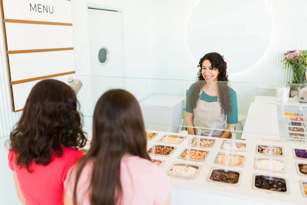 西班牙裔女工一边微笑着 一边和在商店里买冰激凌 冰激凌或冷冻酸奶的少女顾客交谈 — 图库照片