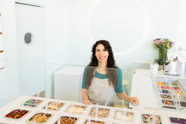 在冷冻酸奶店或冰淇淋店工作的迷人的拉丁女工 在吧台的围裙边微笑着 — 图库照片