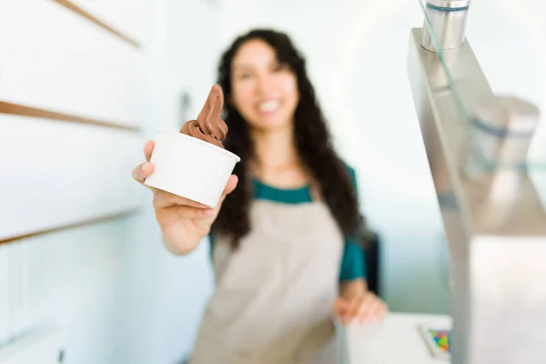 Focus on foreground of a woman worker showing delicious chocolate ice cream at the gelato store or selling frozen yogurt at the store