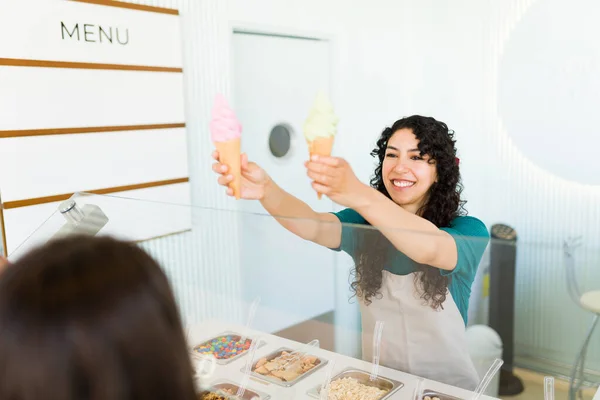 在冷冻酸奶店卖两个冰激凌圆锥给顾客时 快乐快乐的女工笑了 — 图库照片