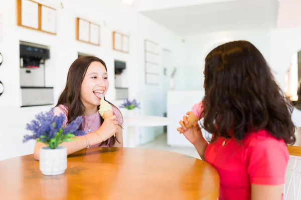 幸せなティーン女の子食べるおいしいアイスクリームコーンと楽しいです親友話しながらでザアイス店一緒に — ストック写真