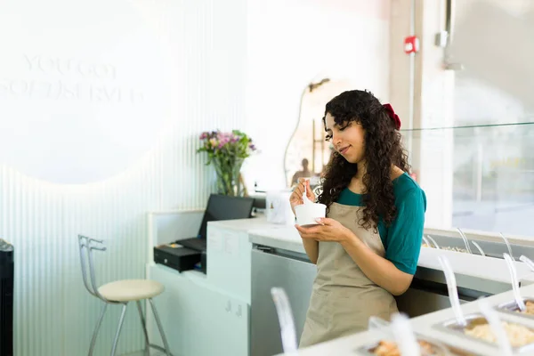 在冰淇淋店工作的年轻女工一边在柜台后面吃着美味的冰冻酸奶一边笑 — 图库照片