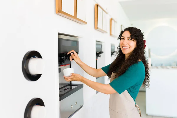 機械のアイスクリームを提供する冷凍ヨーグルト店で働く魅力的な幸せな女性と笑顔作る目の接触 — ストック写真