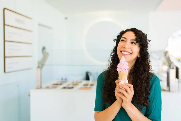 冷凍ヨーグルト店でアイスクリームコーンを食べながら笑っている興奮した若い女性はとても幸せそうに見えます — ストック写真