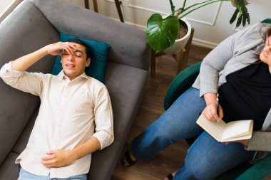 Stresli endişeli adam terapi sırasında koltukta uzanmış depresyon ve endişeden bahsederken yorgun ve üzgün görünüyor.