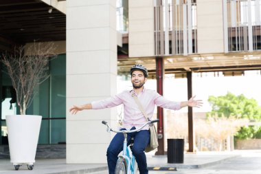 Rahatlamış, kasklı bir iş adamı işe giderken bisiklet sürerken eğleniyor.